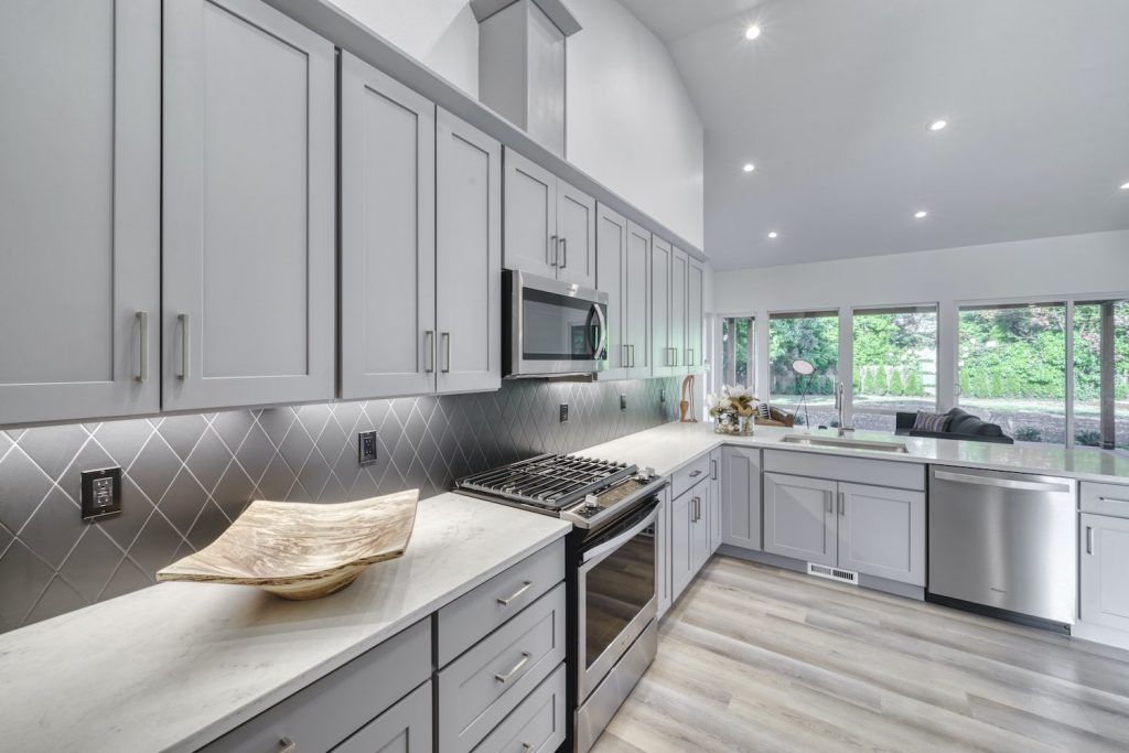Kitchen remodel featuring custom gray cabinetry, white marble counters, and stainless steel appliances
